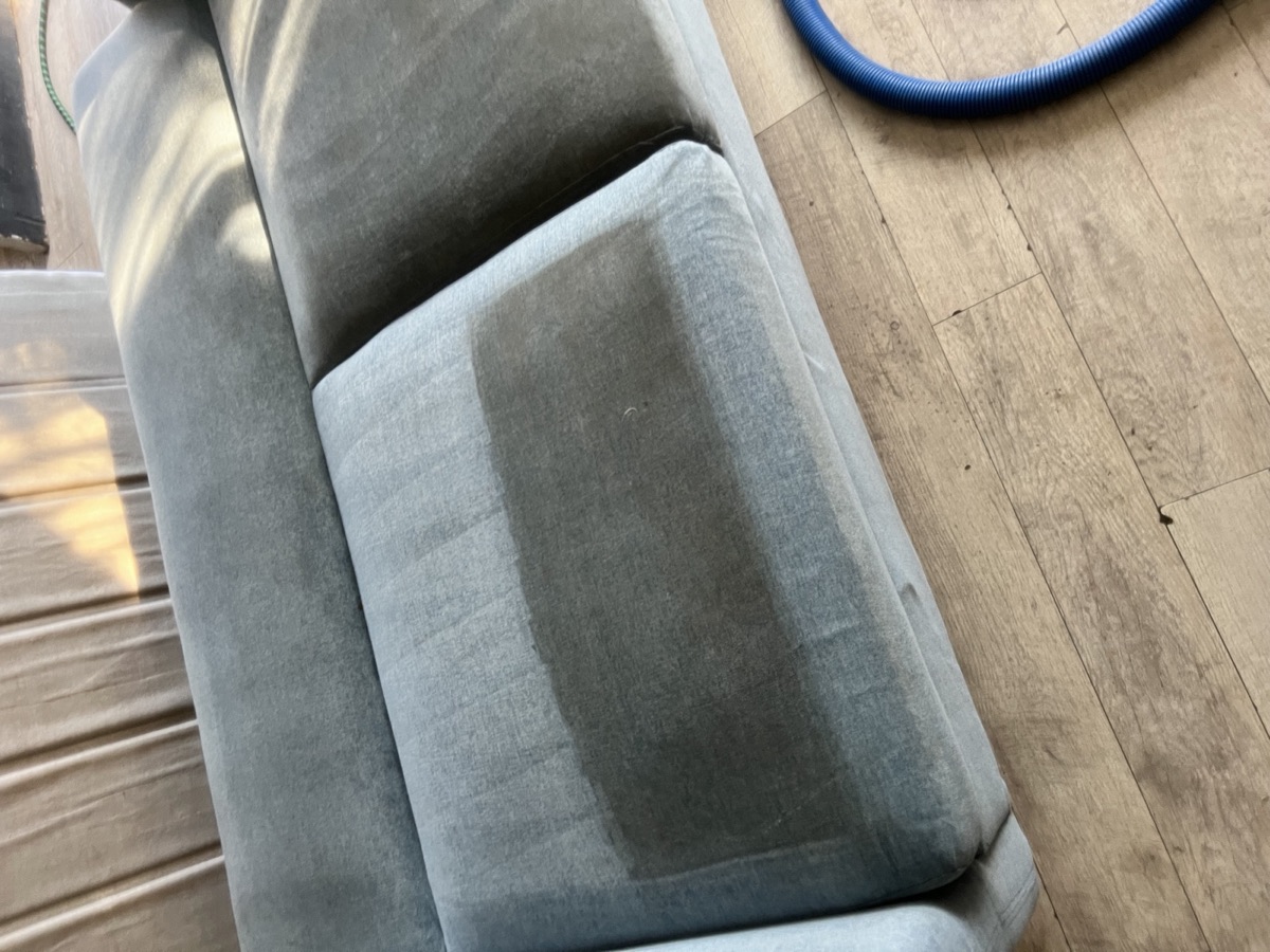 Dark sofa cushion half cleaned showing before and after in one frame